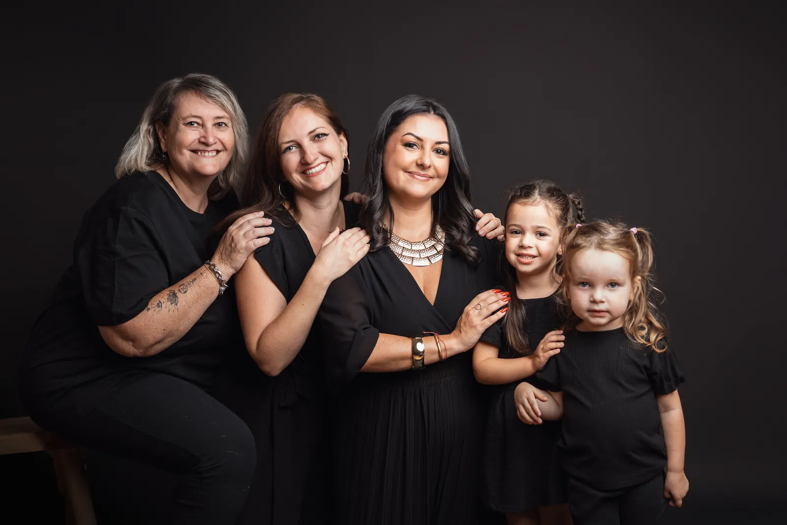 Une grand-mère, ses deux filles et ses deux petites-filles en tenues noires, côte à côte sur fond sombre, dans le studio de Jennifer Venturino à Aix-en-Provence