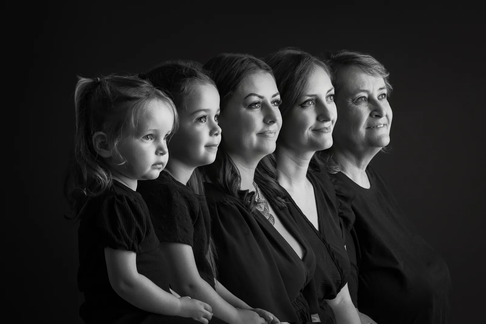 Portrait en noir et blanc de cinq profils alignés sur fond noir : deux petites filles, deux femmes et leur mère