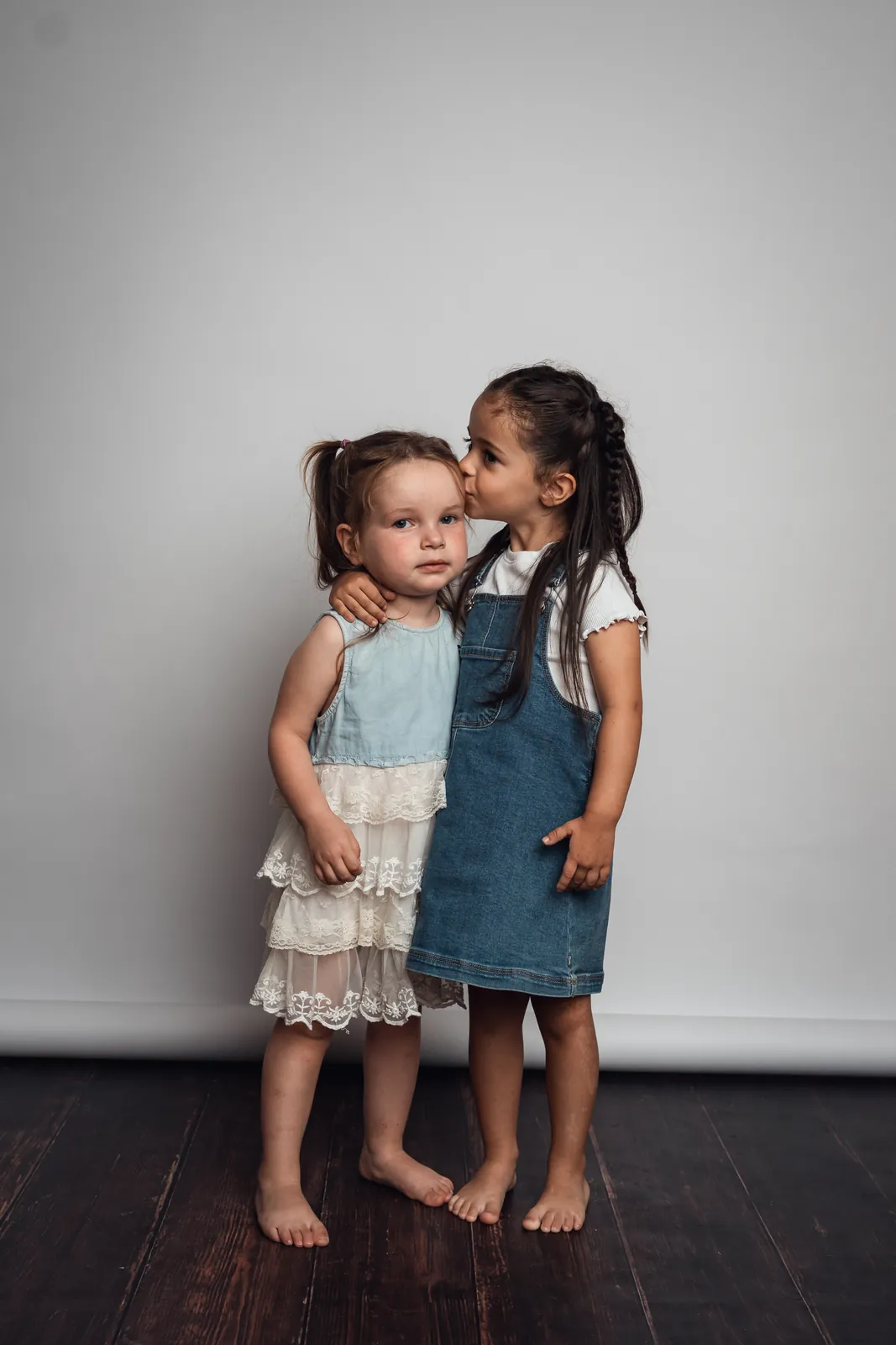 Emmie, avec ses tresses et sa salopette en jean, fait un bisou sur la joue de sa petite cousine Athena, qui regarde l'objectif sans sourire