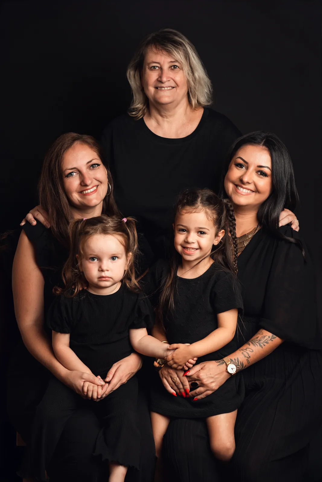 La grand-mère derrière ses deux filles, les deux petites filles devant, toutes en noir sur fond sombre