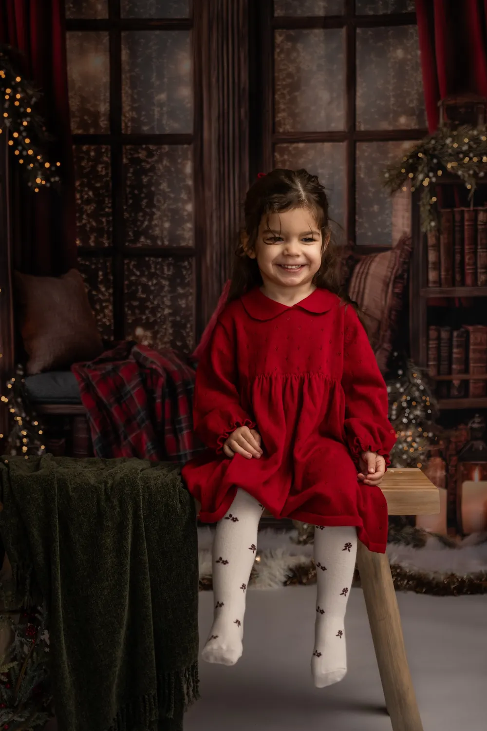 Petite fille souriante assise sur un banc, décor de Noël rouge et vert, mini séance photo de Noël à Aix